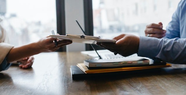 person handing someone a clipboard with a filled out application on it